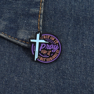 Detailed close-up of religious enamel pin with pray slogans on denim fabric texture