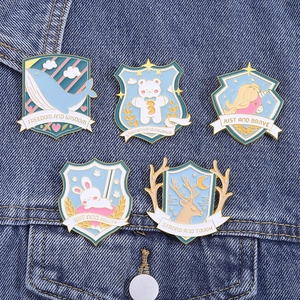 Close-up of enamel pins with animal motifs and quotes on blue denim fabric background
