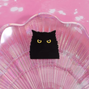 Gros plan d'une broche chat noir en émail avec yeux jaunes sur un décor de coquillage rose