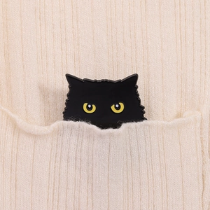 Gros plan d'un badge chat noir en émail avec des yeux jaunes sur un pull tricoté