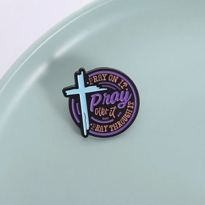 Creative enamel pin with Pray On It cross design on a mint green ceramic plate