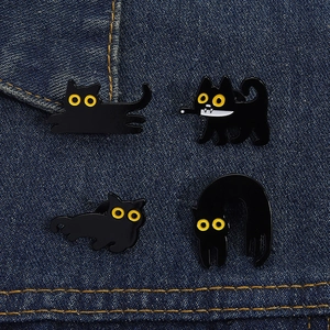 Detailed view of four black cat enamel pins pinned to blue denim fabric showing textures