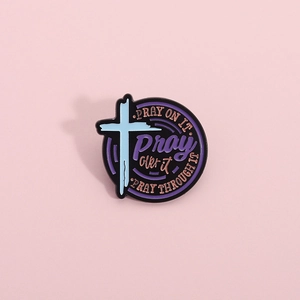 Macro detail of round enamel pin featuring a blue cross and religious prayer text