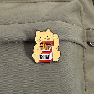 Detail of cartoon yellow cat enamel pin with smoking kills cigarette box on green canvas