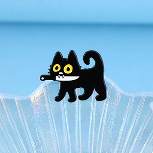 Detail of cute black enamel cat brooch holding a tiny knife on a shell background