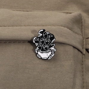 Detail of creative black cat enamel pin emerging from a white coffee cup on canvas material