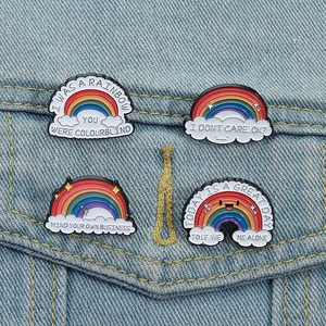 Enamel rainbow pins set with cloud and text designs on blue denim jacket fabric