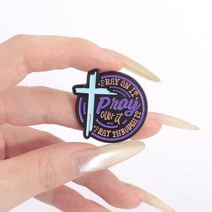 Detail of round enamel pin with cross pattern and Pray on it inspirational quotes