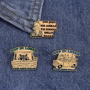 Close-up of three cartoon enamel pins with humorous quotes on blue denim fabric