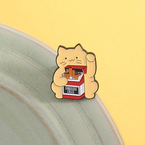Detailed macro view of an enamel cat pin holding a red cigarette box on yellow background