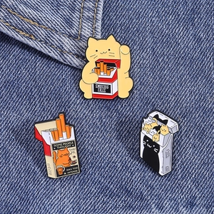 Macro shot of three quirky cartoon cat enamel pins on dark blue denim fabric texture