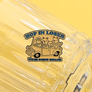 Detail of enamel lapel pin showing cartoon bears driving with Hop In Loser slogan