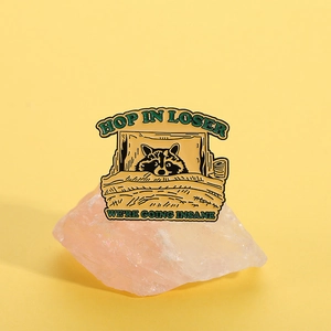Detail of enamel pin featuring a raccoon in bed with Hop In Loser We're Going Insane text