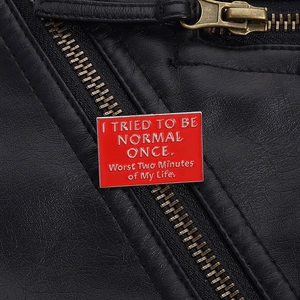 Macro shot of red enamel pin with humor text pinned on a black leather jacket detail