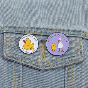 Détail de deux pins en émail canard sur veste en jean avec citations et motifs mignons