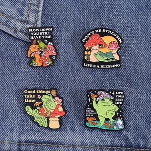 Détail de quatre épingles en émail avec grenouilles et champignons sur une veste en jean bleue