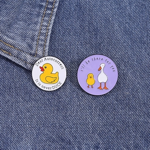 Vue détaillée de deux pin's ronds en émail avec motifs d'oie sur tissu denim bleu