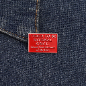 Detail of red enamel brooch with humorous quote pinned on blue denim fabric