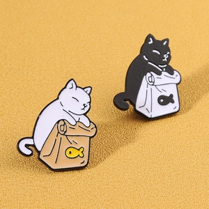 Süße Emaille-Pins mit schwarz-weißen Katzenmotiven auf Papiertüten mit Fischmuster