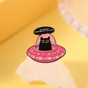 Detail einer Emaille-Brosche mit schwarzer Katze im UFO und spanischem Text