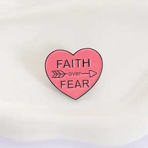 Macro detail of heart enamel pin with Faith over Fear text and arrow design