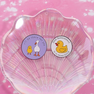 Gros plan de badges en émail canard sur plateau coquillage rose aux détails fins