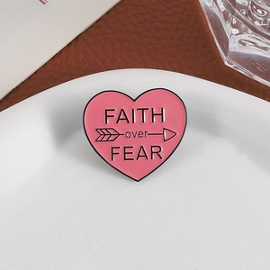 Detail of pink heart enamel pin with FAITH over FEAR text on a white ceramic plate