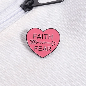 Macro detail of a pink heart enamel pin featuring FAITH over FEAR text on canvas