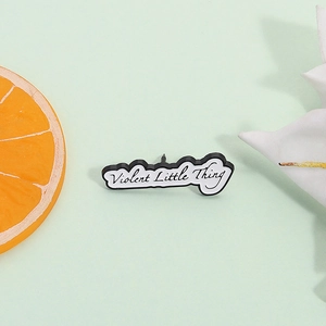 Minimalist enamel brooch with Violent Little Thing text on a textured green background