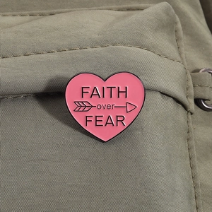 Close-up of pink heart enamel pin with Faith Over Fear text on olive canvas bag