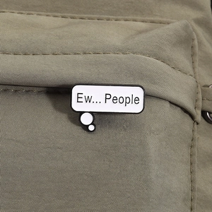 Detail shot of Ew... People speech bubble enamel pin on olive green fabric