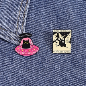 Detail von Emaille-Pins mit UFO und schwarzer Katze auf blauem Denim-Stoffgewebe