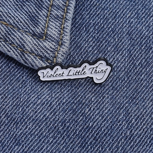 Gros plan du pin's en émail Violent Little Thing sur une texture denim bleu foncé