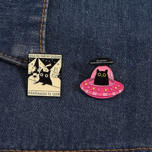 Detailansicht der Emaille-Pins mit schwarzer Katze und UFO auf blauem Denim-Stoff