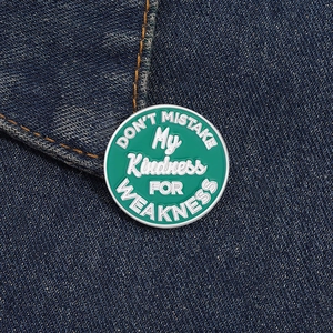 Dettaglio della spilla smaltata verde tonda con citazione motivazionale su denim