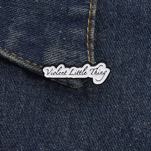 Détail d'un pin's émaillé blanc avec lettrage noir sur une veste en jean bleue