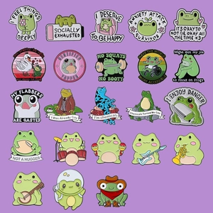 Flat lay grid display showing various funny frog enamel pins on a purple background