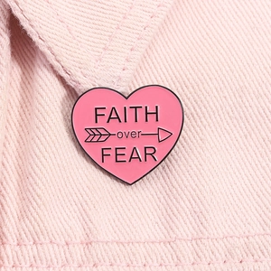 Close-up of pink heart enamel pin with FAITH over FEAR text on denim fabric