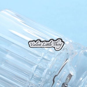 Gros plan du badge en émail Violent Little Thing sur une surface en verre texturé