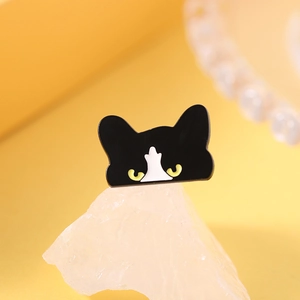 Macro shot of a cute black and white enamel cat pin on a decorative white stone