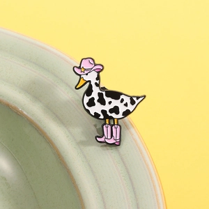 Detailed view of a cartoon enamel duck pin with cow print patterns and pink cowboy boots