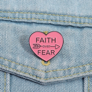 Pink heart enamel pin with Faith Over Fear text on blue denim jacket pocket