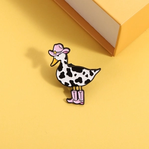 Detailed view of enamel duck pin with cow print patterns wearing pink cowboy boots