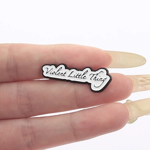 Detail of hand-held enamel brooch featuring handwritten Violent Little Thing text