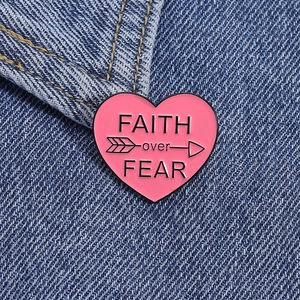 Detail of pink enamel heart brooch with FAITH over FEAR text on blue denim jacket