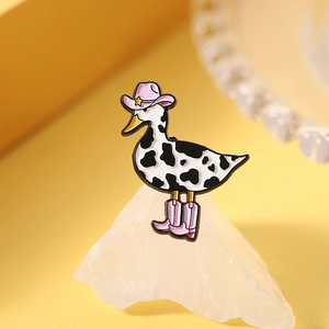 Detail of creative cow-print duck enamel pin with pink cowboy hat and boots on yellow background
