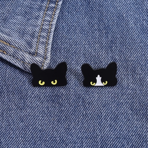 Cute black and white enamel cat pins displayed on a denim fabric background
