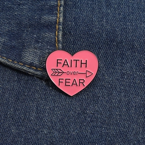 Detail of pink heart enamel pin with FAITH over FEAR text on blue denim jacket fabric