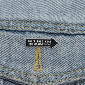Detailed close-up of a black arrow enamel pin featuring inspirational text on denim fabric