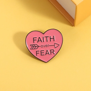 Pink heart enamel pin with 'FAITH over FEAR' slogan on a bright yellow background